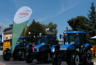 trzy nowe niebieskie traktory stojące na dożynkach