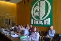 uczestnicy konferencji siedzący przy stole nad nimi zawieszony na ścianie duży znak IHAR